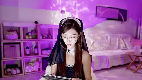 Media: Video of an Asian woman dressed as a sexy nun, sitting in a dimly lit bedroom with purple lighting, wearing glasses, reading a tablet.