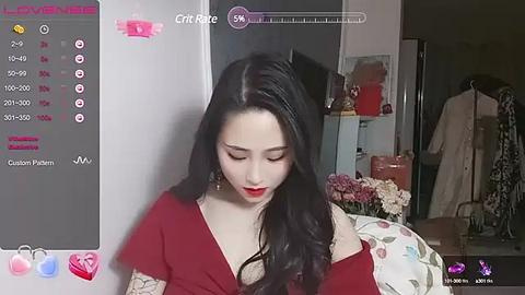 Media: A video of an East Asian woman with long black hair, wearing a red off-shoulder dress, standing in a dimly lit room with a floral-patterned tablecloth.