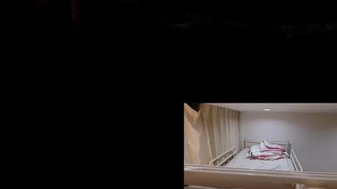 Media: Video of a dimly lit, sparsely furnished hospital room with a single bed, white sheets, and a red blanket. The room's walls are painted light beige, and there is a small, bright light fixture in the ceiling.