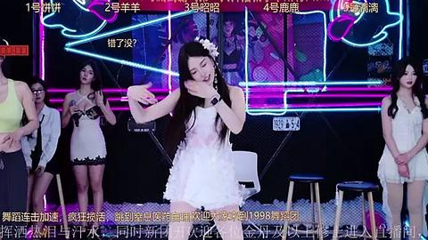 Media: Video of a female singer in a white dress, performing on stage with neon lights. She has long black hair adorned with a flower, surrounded by other performers.