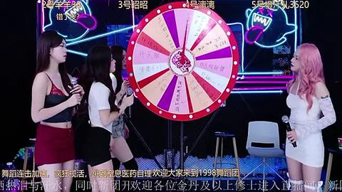 Media: Video of four women, two with long hair and two with short hair, singing into microphones on stage. A large roulette wheel with Chinese numbers spins in the background.