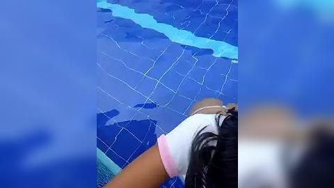 Media: Video of a person's upper body in a white polo shirt, leaning over a blue swimming pool with a white grid pattern, blurry background.