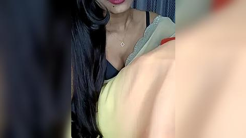 Media: A video of a woman with long black hair and fair skin, wearing a black bra and a light green top, leaning over a person, blurred.