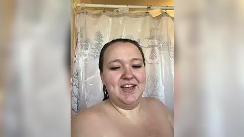 Media: Video of a smiling, topless woman with wet hair, wearing a clear shower cap, standing in a shower with a floral-patterned curtain.