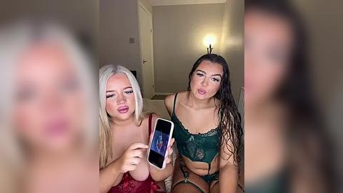 Media: Video of two women, one with blonde hair, the other brunette, both in lingerie, holding a smartphone, capturing a blurred background.