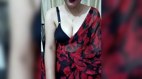 Media: Video of a woman with fair skin wearing a black bra under a red and black floral-patterned sari. She has a slender figure and is indoors, with a blurred background.