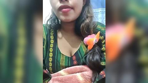 Media: Video of a South Asian woman with medium brown skin, wearing a green and yellow striped blouse with a flower hair accessory, holding a pink towel.