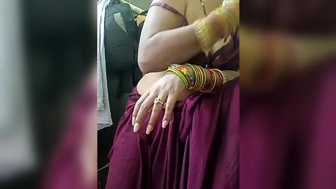 Media: Video of an Indian woman in traditional attire, a maroon sari with gold jewelry, seated in a car. She has a fair complexion and is wearing several bangles.