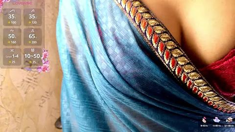 Media: Video of a draped blue sari with intricate golden embroidery on the border, showcasing a woman's bare shoulder and a red blouse peeking out. Background features a digital map and health data display.