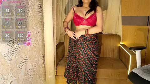 Media: Video of a woman with medium skin tone, wearing a red lace bra and black floral pants, standing in a modern, beige-lit room with a wooden chair and decorative wall art.