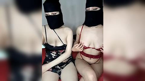 Media: Video of two Asian women with fair skin, wearing black masks, red lace lingerie, and black floral lingerie, sitting side by side on a red couch.