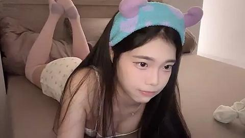 Media: A video of an East Asian woman with long black hair, wearing a blue animal-themed headband, lying on her stomach in pajamas on a beige couch.