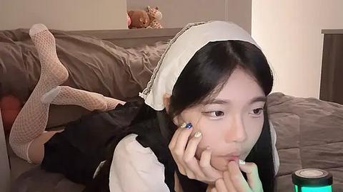 Media: Video of an Asian woman in a French maid outfit lying on a bed, holding a banana, with a stuffed bear and a green can in the background.