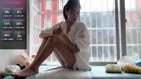 Media: Video of an East Asian woman with fair skin, sitting on a bed with a white robe, checking a \"Love Meter\" app on her phone, in a bright, modern room with large windows.