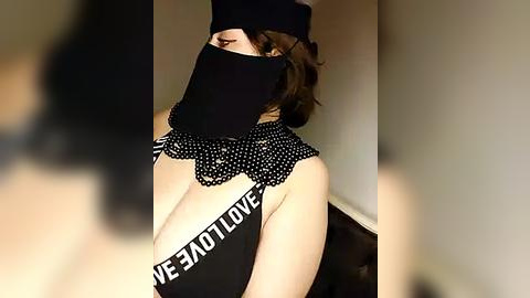 Media: Video of a woman with light skin and medium brown hair, wearing a black mask, black headband, and black top with white \"Venus\" text, standing indoors against a neutral background.