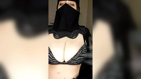 Media: Video of a woman with light skin, wearing a black face mask, black striped bra revealing ample cleavage, and black hooded jacket.