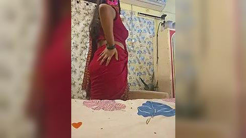 Media: A video of a woman in a red sari standing in a room with floral wallpaper, an air conditioner, and a blue chair.