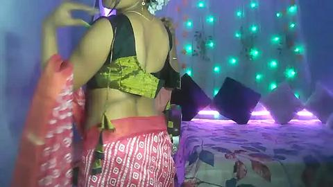 Media: Video of a woman in a colorful, patterned skirt and black crop top, dancing in a dimly lit room with blue and green LED lights.