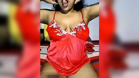 Media: Video of a South Asian woman in a red satin lingerie top, playfully sticking her tongue out, hands on her head, in a bedroom with blurred red curtains.