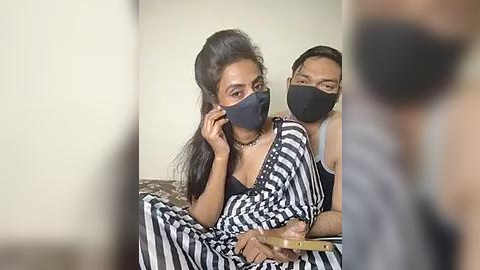 Media: Video of two people in a bedroom; a woman with dark hair and a mask, and a man with a mask, wearing black and white striped attire.