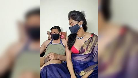 Media: Video of a man and woman in traditional attire wearing masks, sitting on a bench, with a blurred background.