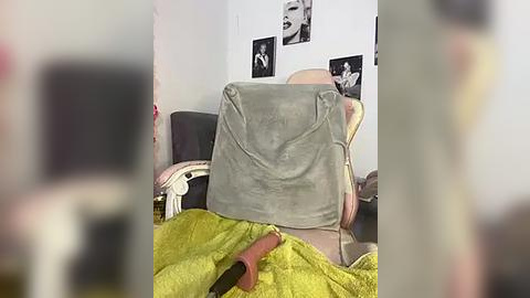 Media: Video of a person reclining in a chair, covered with a lime-green blanket, wearing a beige hat. Background features black-and-white Marilyn Monroe posters on a white wall.