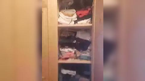 Media: A video of a tall, narrow wooden closet with three shelves, filled with neatly folded clothes, towels, and miscellaneous items, including a red bag and white laundry basket.