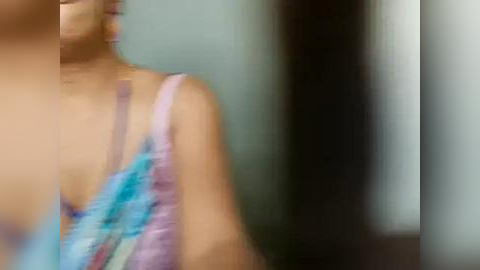 Media: Blurry video of a woman with light skin, wearing a pastel blue bralette, standing indoors against a blurred background. The image is out of focus.