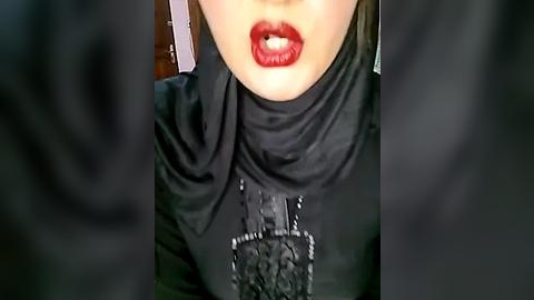 Media: Video of a close-up of a woman's face, showcasing bold red lipstick, a black hijab, and a detailed black lace headpiece with intricate patterns.