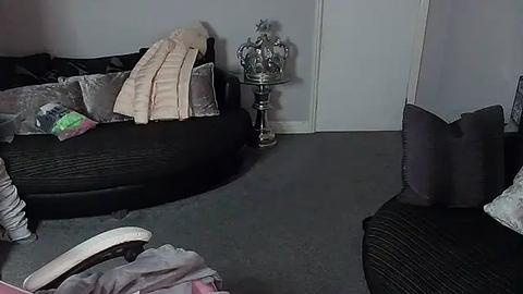 Media: A video of a messy living room with two black couches, a gray carpet, a silver candle holder, and a pink blanket.