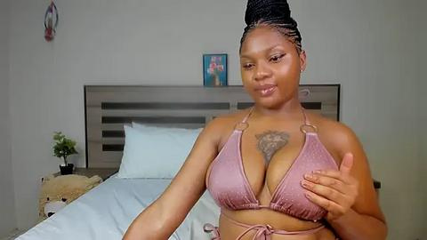 Media: Video of a curvy Black woman with medium skin tone, wearing a pink bikini, large breasts, and a lion tattoo on her chest, standing in a modern bedroom.