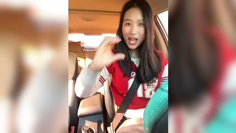 Media: Video of a young Asian woman with long black hair, wearing a red and white varsity jacket, sitting in a car with a seatbelt.