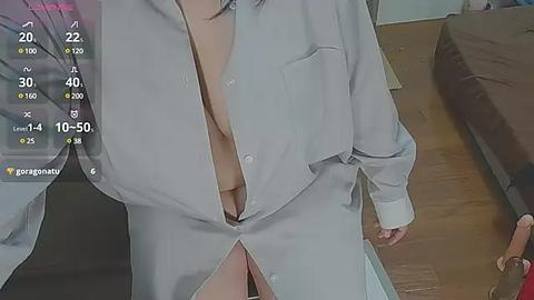 Media: Video of a light-skinned woman wearing an unbuttoned white shirt, exposing her black bra. Background features a wooden floor, a bed, and a person partially visible.