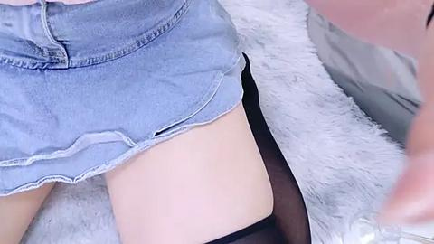 Media: Video of a person's lower leg in light denim shorts and black sheer thigh-high stockings, lying on a white, fluffy rug.