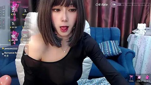 Media: Video of an Asian woman with straight black hair, wearing a sheer black top, sitting on a blue couch in a dimly lit room, surrounded by a virtual camera interface.