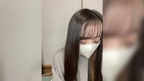 Media: A video of an Asian woman with long black hair and a white face mask, standing in a dimly lit room with beige walls and a wooden door.