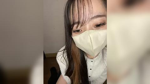 Media: A video of an Asian woman with long, straight hair, wearing a white mask and a white blouse, taken from a low angle, showing her face and upper torso.