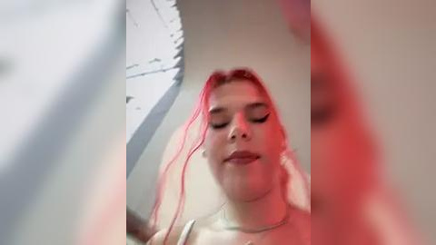 Media: Video of a young woman with long, pink hair, closed eyes, and a slight smile, taken from a low angle, showing off her slim figure.