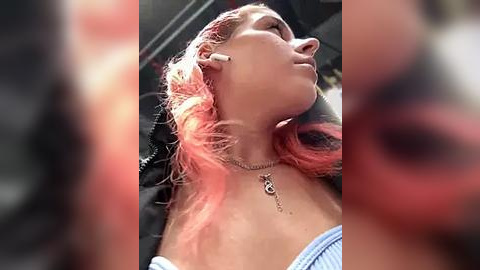 Media: Video of a young woman with pink hair, wearing a black jacket and a blue off-shoulder top, leaning back in a car with her head tilted up, earbuds in.