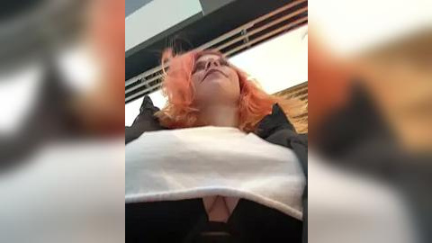 Media: A video of a woman with shoulder-length, vibrant pink hair, wearing a black jacket over a white top, captured from a low angle, emphasizing her chest.