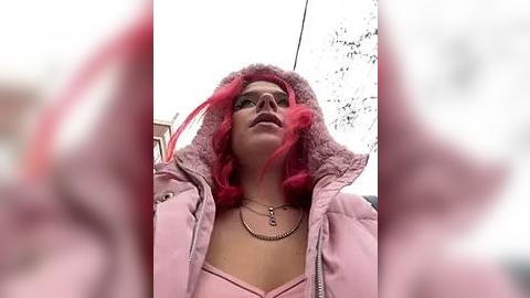 Media: Video of a young woman with pink hair, wearing a pink jacket and a pink hood, standing outside with blurred background.