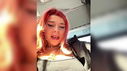 Media: Video of a young woman with bright pink hair, wearing black clothing, and makeup, taken from a moving car, blurry background.