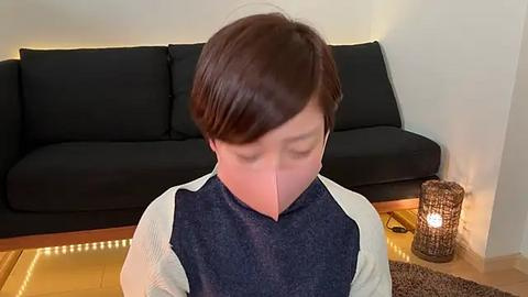 Media: A video of a young boy with short brown hair, wearing a navy-blue shirt with white sleeves, sitting on a wooden floor. He's in a modern living room with a black couch, a wooden coffee table, and a candle-lit wicker lantern.