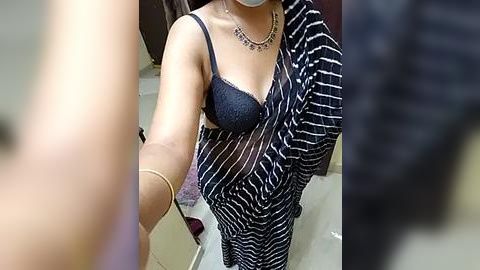 Media: Video of a woman with medium skin tone, wearing a black lace bra and black and white striped saree, standing in a bathroom with beige tiles.