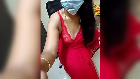 Media: Video of a pregnant woman in a red lace lingerie top, light blue face mask, and gold bracelet, sitting in a black chair.