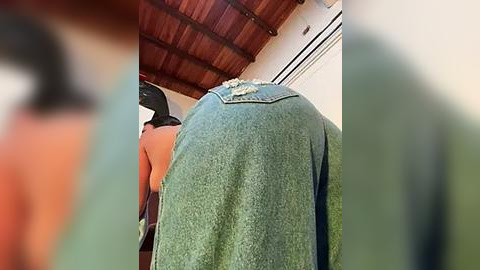 Media: Video of a woman's backside in tight, distressed denim shorts, leaning over a wooden table. Her skin tone is medium, and she's wearing a black top. Background includes wooden ceiling beams and white walls.