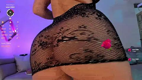 Media: Video of a curvy woman with a large, round buttocks in a black, fishnet mini skirt with a rose. Background features a purple light and a gaming screen.