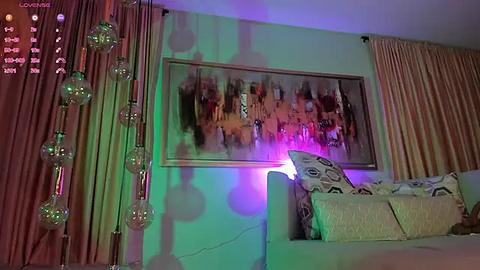 Media: Video of a modern bedroom with a large abstract painting on a pale green wall, illuminated by soft purple and green lights. The bed features patterned pillows and a sheer curtain to the right.