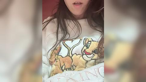 Media: A video of a person wearing a The Lion King-themed T-shirt with Simba and Nala, lying on a bed with a blurred background.