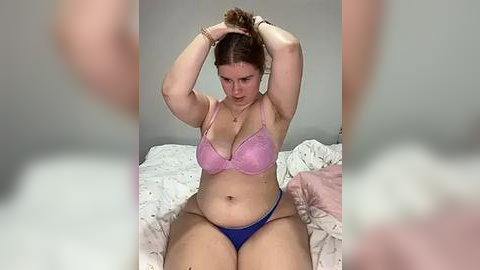 Media: A video of a plus-sized woman with light skin, brown hair, and a pink bra and blue panties, sitting on a bed with white sheets, adjusting her hair.